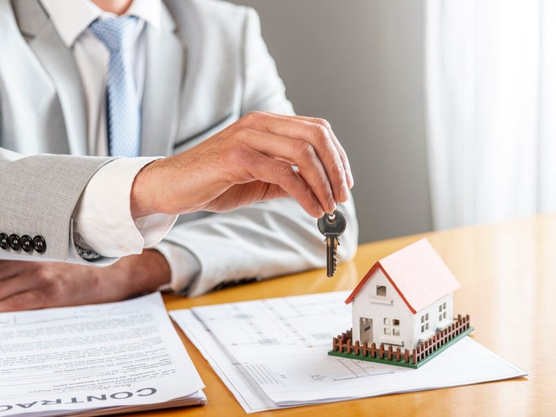 person-holding-house-keys-toy-model-house-desk_23-2148301737