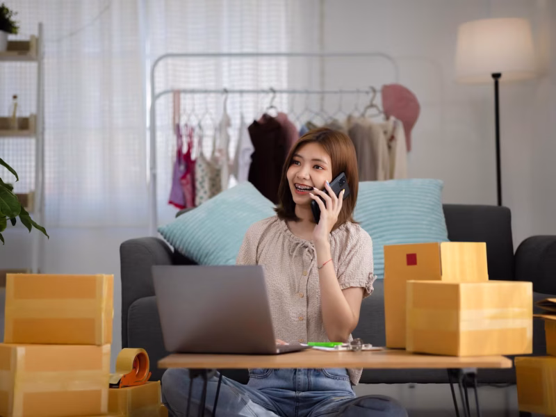 smiling-happy-young-asian-woman-entrepreneur-receiving-phone-call-new-sales-order-boxes-product-with-laptop-computer_658552-53